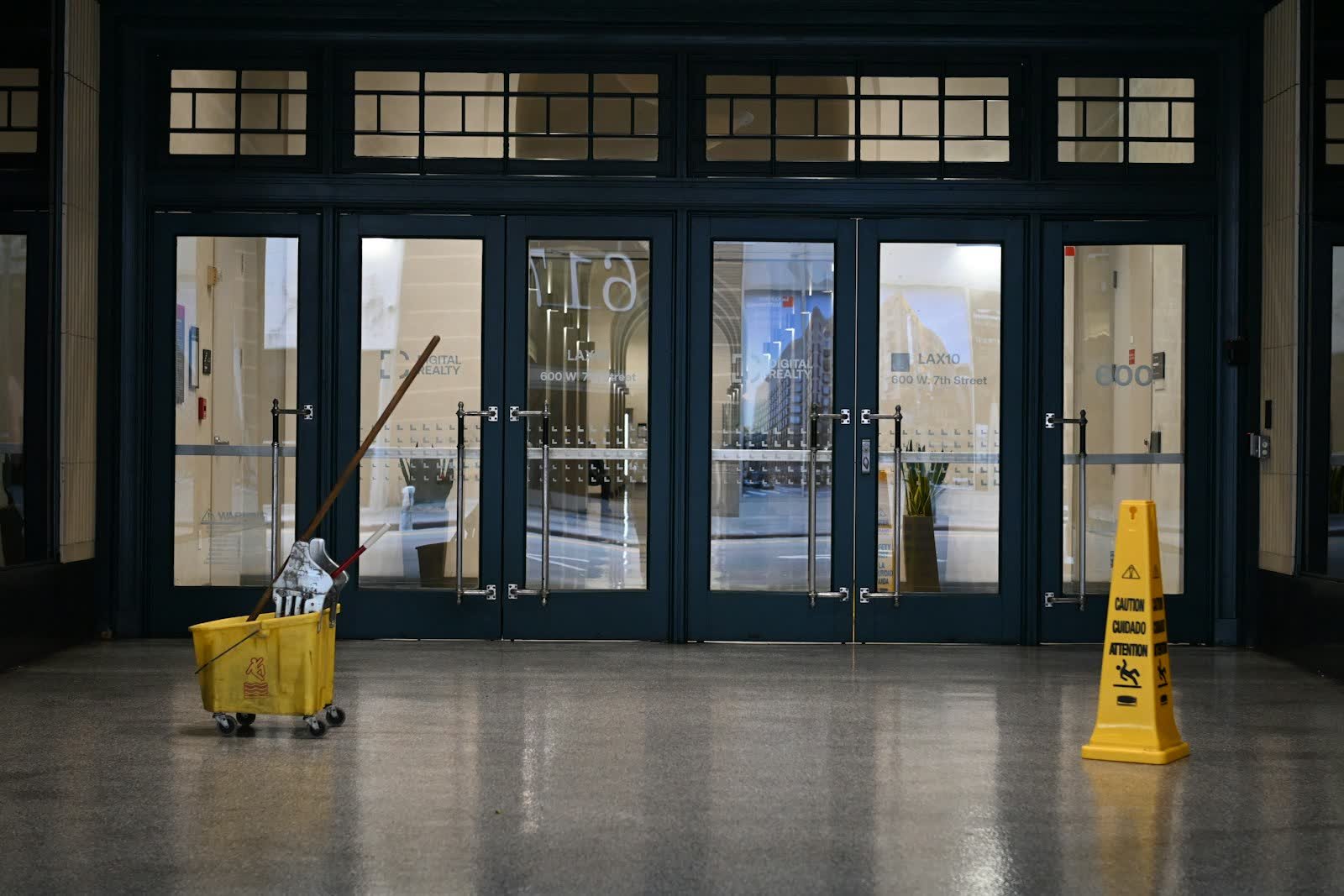 A mop bucket and wet floor sign inside glass entrance doors
